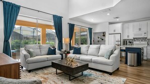 A modern living room with a sofa, coffee table, and large windows with curtains. - MEGA HOME! Relax By the Pool! EPIC Resort-Only 4 miles to Disney! (Kissimmee)