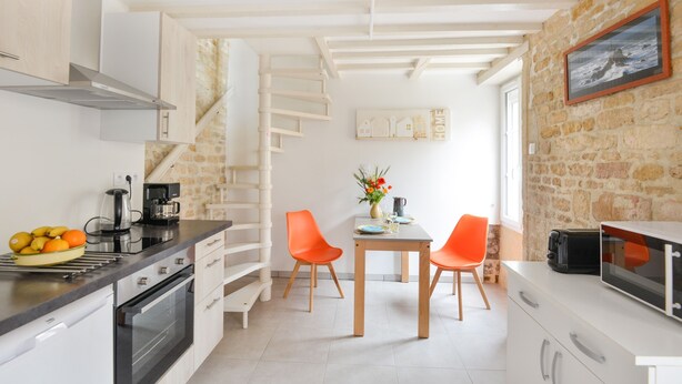 Ett modernt kök med vita skåp, en inbyggd ugn och en matplats med två orangefärgade stolar.