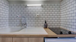 Une cuisine moderne avec des carreaux de céramique blancs disposés en motif métro, un plan de travail en bois, un évier en acier inoxydable, un robinet, un distributeur de savon et une cuisinière encastrée.