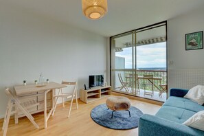A modern living room with a wooden dining table, chairs, a TV, and a sofa. - L'Écrin d'Elteville - Charmant studio (Montrichard Val de Cher)