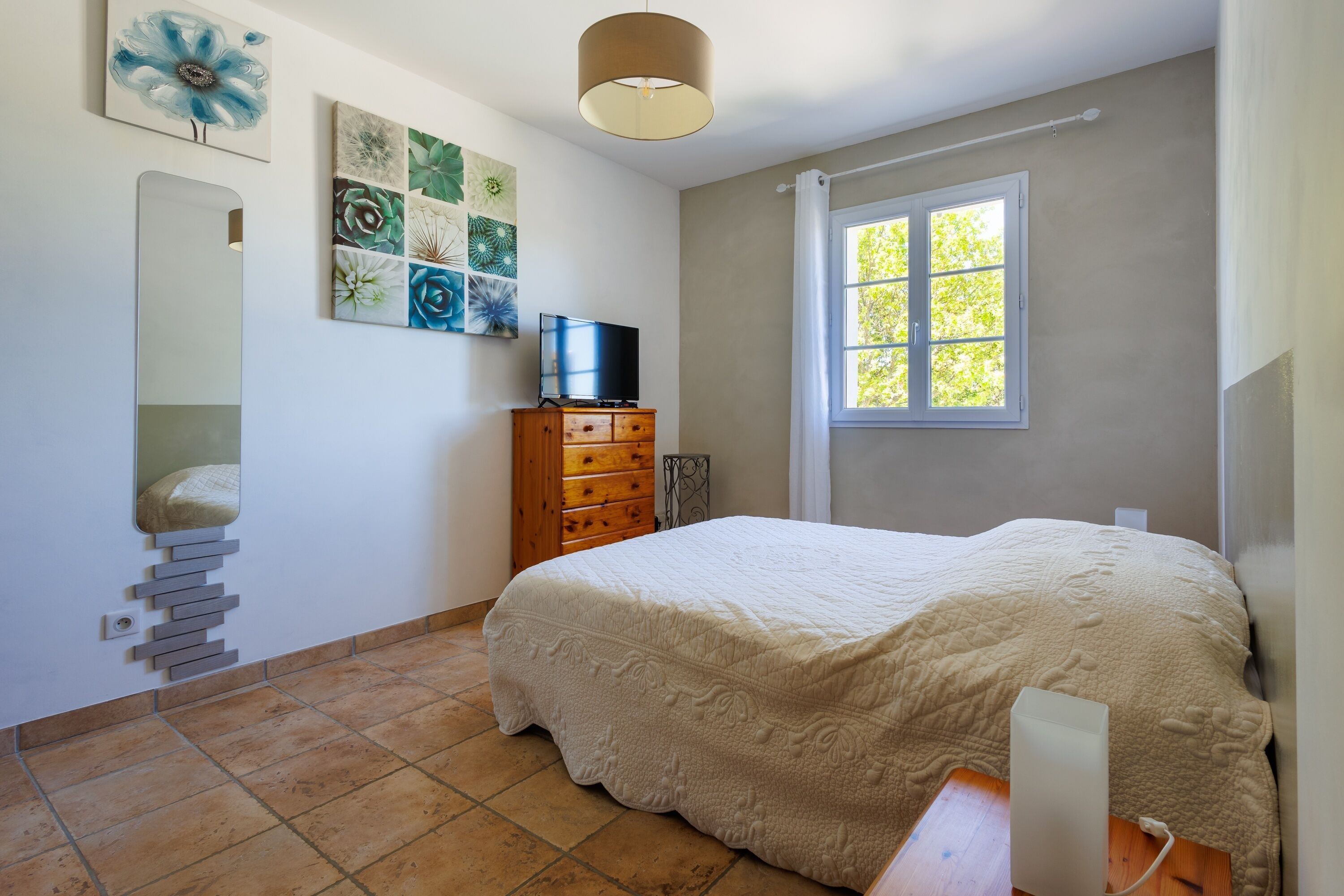 Een slaapkamer met een bed, een dressoir, een televisie en kunst aan de muur.