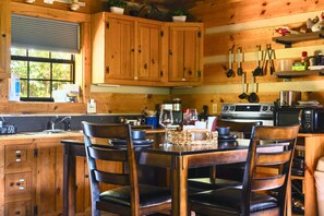 A wooden cabin interior with a dining table, chairs, kitchen appliances, and a window with blinds. - Point of View Cabin · Private Hot Tub, Fire Pit & Mountain Views · Dog-Friendly (Sevierville)