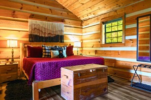 A log cabin bedroom with a wooden bed, a nightstand, a dresser, a window with a view, and a hanging tapestry. - Point of View Cabin · Private Hot Tub, Fire Pit & Mountain Views · Dog-Friendly (Sevierville)