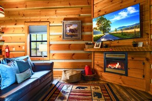 A cozy cabin interior with a fireplace, a television, a sofa, and a window. - Point of View Cabin · Private Hot Tub, Fire Pit & Mountain Views · Dog-Friendly (Sevierville)