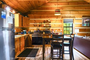 A cabin-style kitchen with wooden walls, a refrigerator, stove, and a dining area with chairs. - Point of View Cabin · Private Hot Tub, Fire Pit & Mountain Views · Dog-Friendly (Sevierville)