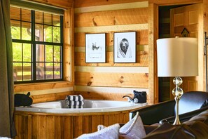 A wooden cabin interior with a bathtub, two framed pictures, and a lamp. - Point of View Cabin · Private Hot Tub, Fire Pit & Mountain Views · Dog-Friendly (Sevierville)