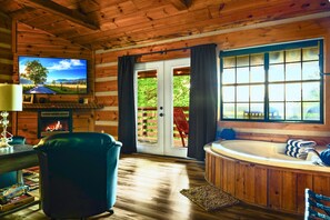 A cabin interior with a fireplace, a television, a large window, and a hot tub. - Point of View Cabin · Private Hot Tub, Fire Pit & Mountain Views · Dog-Friendly (Sevierville)