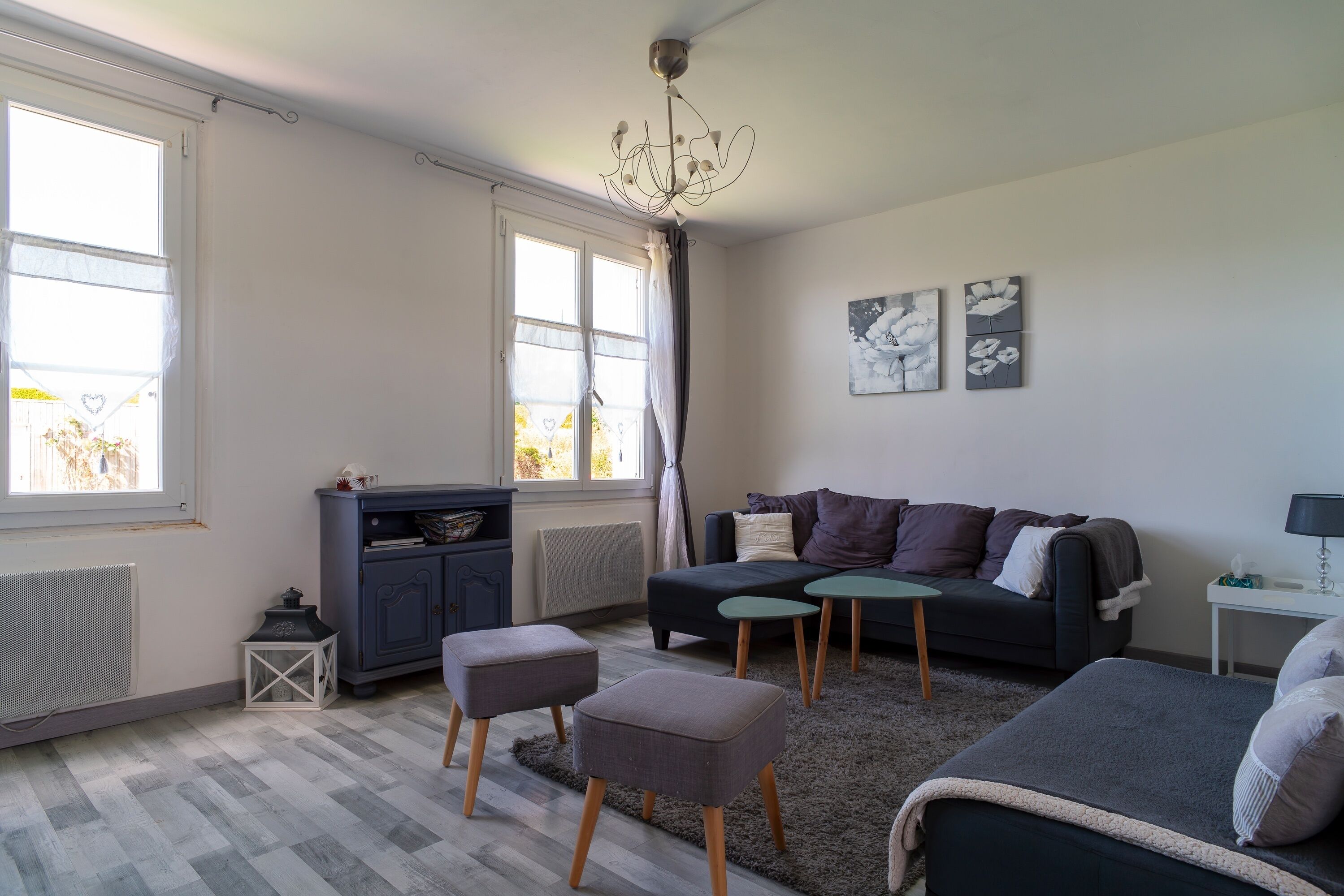 Un salon moderne avec un canapé, des poufs, une petite table et un radiateur.