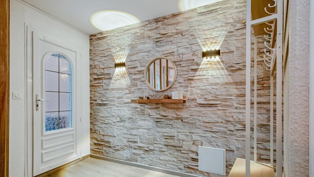 Un pasillo con pared de piedra, una puerta blanca con panel de vidrio esmerilado y dos luces fijadas a la pared.