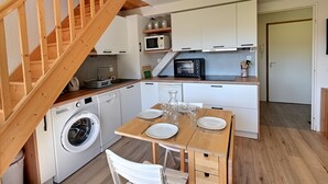 A compact kitchen with a washing machine, microwave, and wooden dining table set for four. - Le Nid des Vosges - Appt vue montagne (Gérardmer)