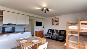 A compact living space with a kitchenette, a dining area, a sofa, and a bunk bed. - Le Nid des Vosges - Appt vue montagne (Gérardmer)