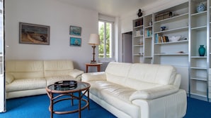 A living room with a white leather sofa, a glass coffee table, and a bookshelf.