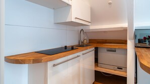 A modern kitchen with white cabinetry, a wooden countertop, a built-in dishwasher, and a stainless steel faucet. - La Timonerie - Studio climatisé à Bénodet (Benodet)