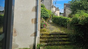 Un edificio de piedra con aspecto rústico, un pequeño jardín con flores y un cielo azul despejado.