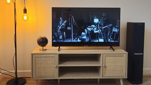 Un televisor sobre un mueble de madera con un globo encima, una lámpara de pie con tres bombillas y un altavoz a la derecha.