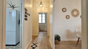 Un pasillo con suelo de madera, una lámpara en el techo, un refrigerador y una silla.