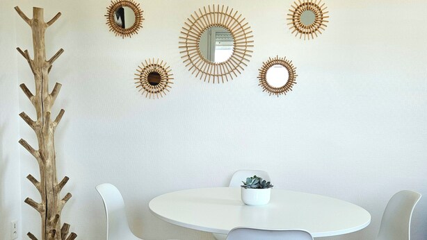 Un comedor con una mesa redonda blanca, cuatro sillas blancas y una escultura de árbol de madera.