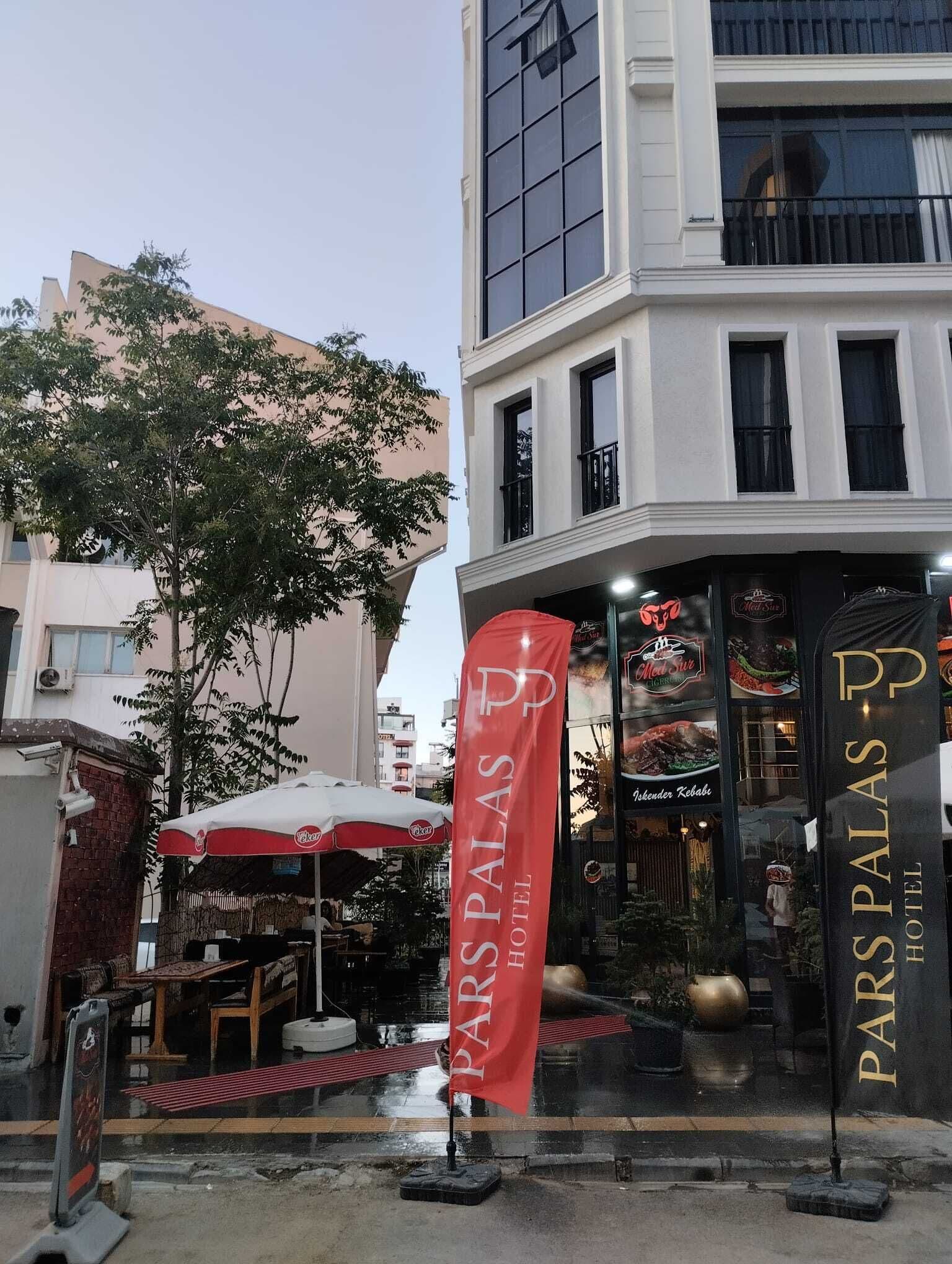 A hotel entrance with a red flag, outdoor seating, and a view of the street.