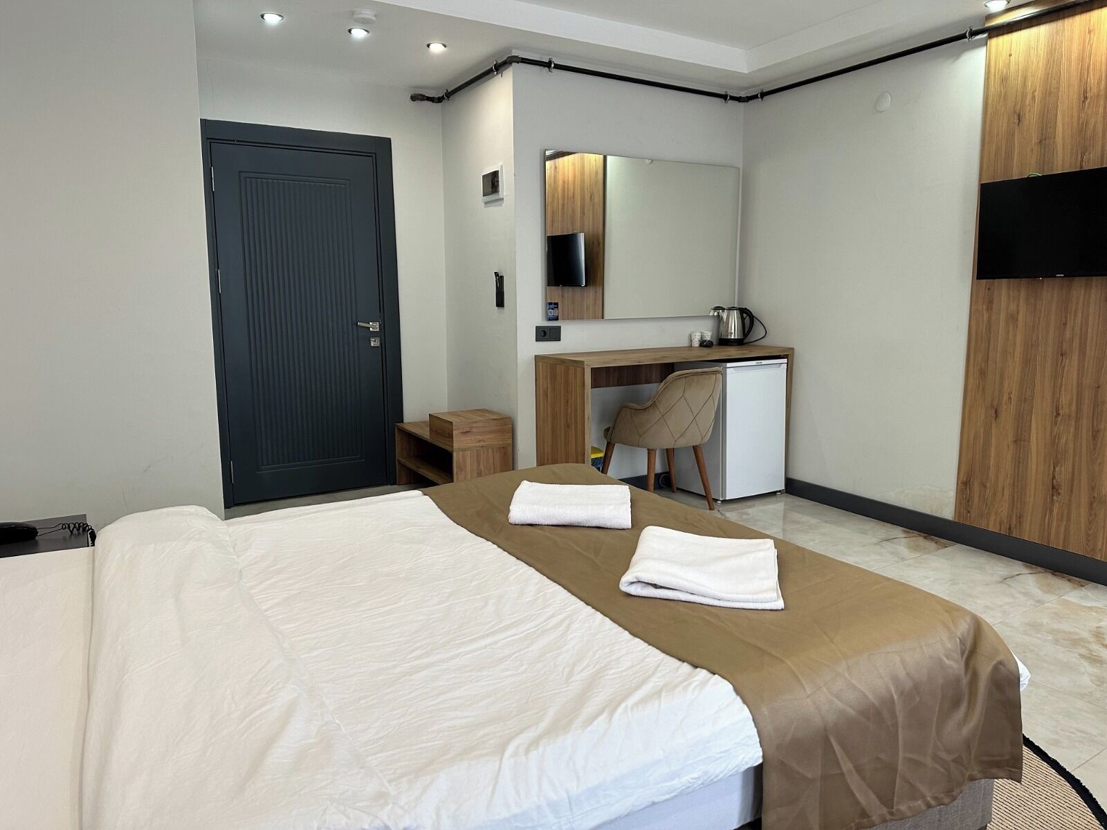 Een hotelkamer met een bed, een bureau, een stoel, een klein kastje, een spiegel en een televisie.