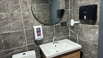 Un baño con lavamanos blanco, un espejo, un inodoro y un secador de manos.