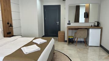 A hotel room with a bed, a desk, a chair, a small refrigerator, and a mirror.