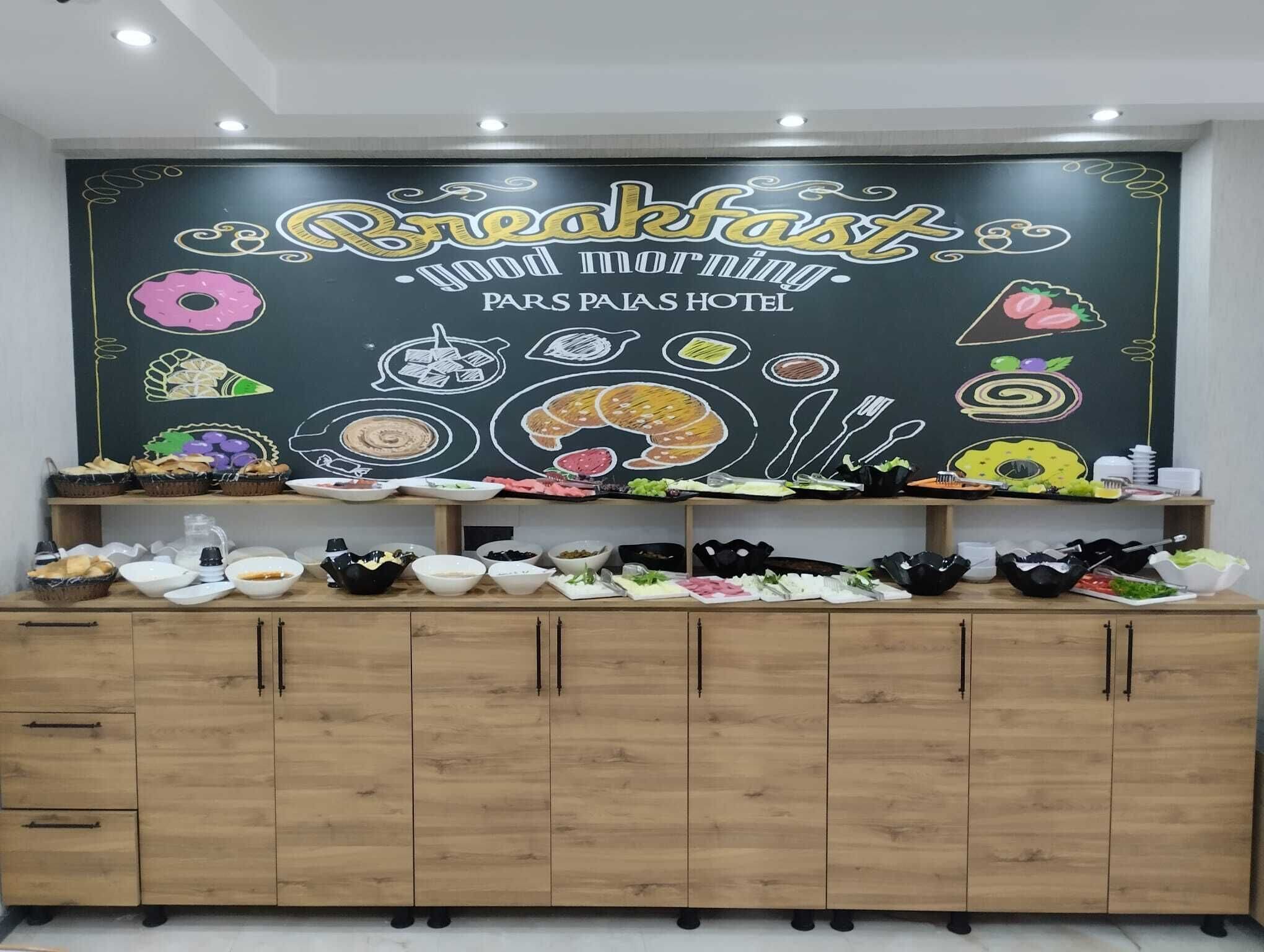 A breakfast buffet setup with a chalkboard sign reading "Breakfast good morning" and "PARS PALAS HOTEL".