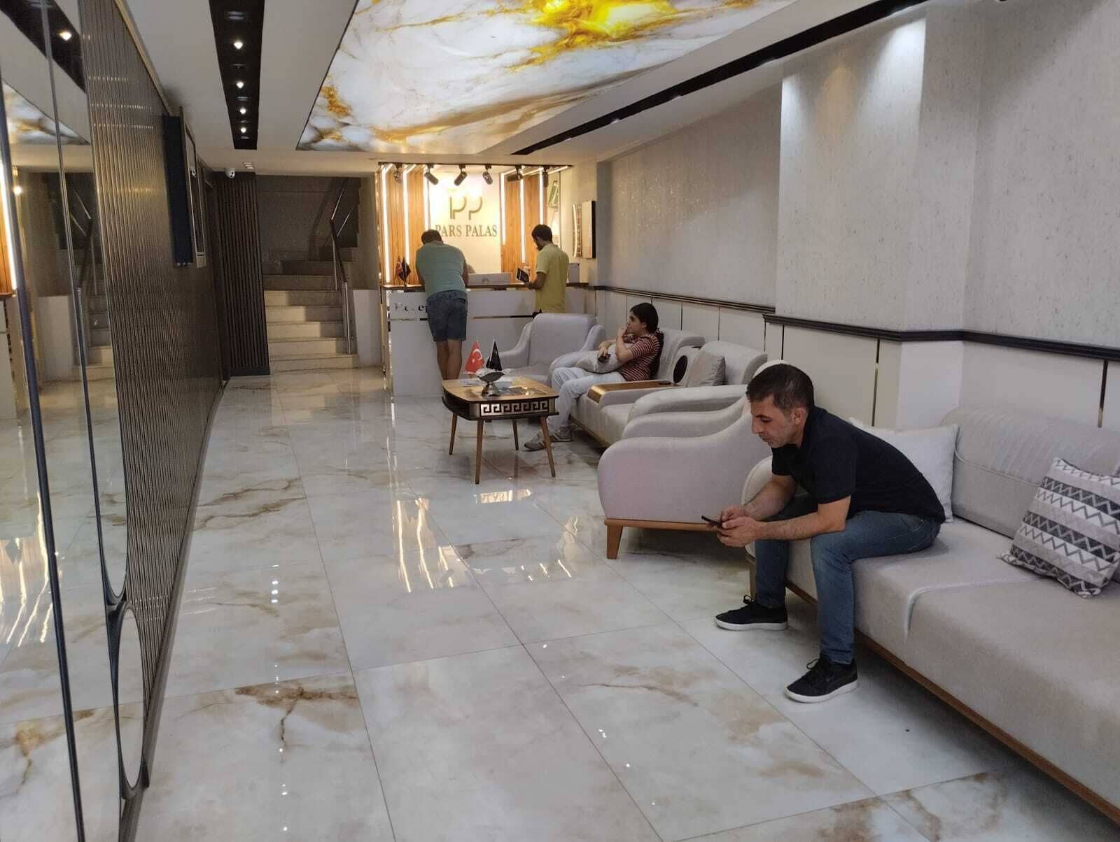 A modern hotel lobby with a marble floor, a reception desk, and seating areas.