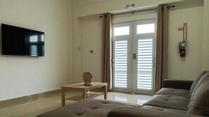 Un soggiorno con divano, televisore, un tavolino con un oggetto decorativo e una porta finestra con tende.