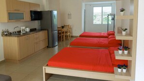 Camera d'albergo compatta con angolo cottura, un letto con biancheria rossa, un'area pranzo e una finestra con persiane.