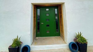 Ein Haus mit grüner Tür, einer kleinen Veranda und je einem Blumentopf auf beiden Seiten.