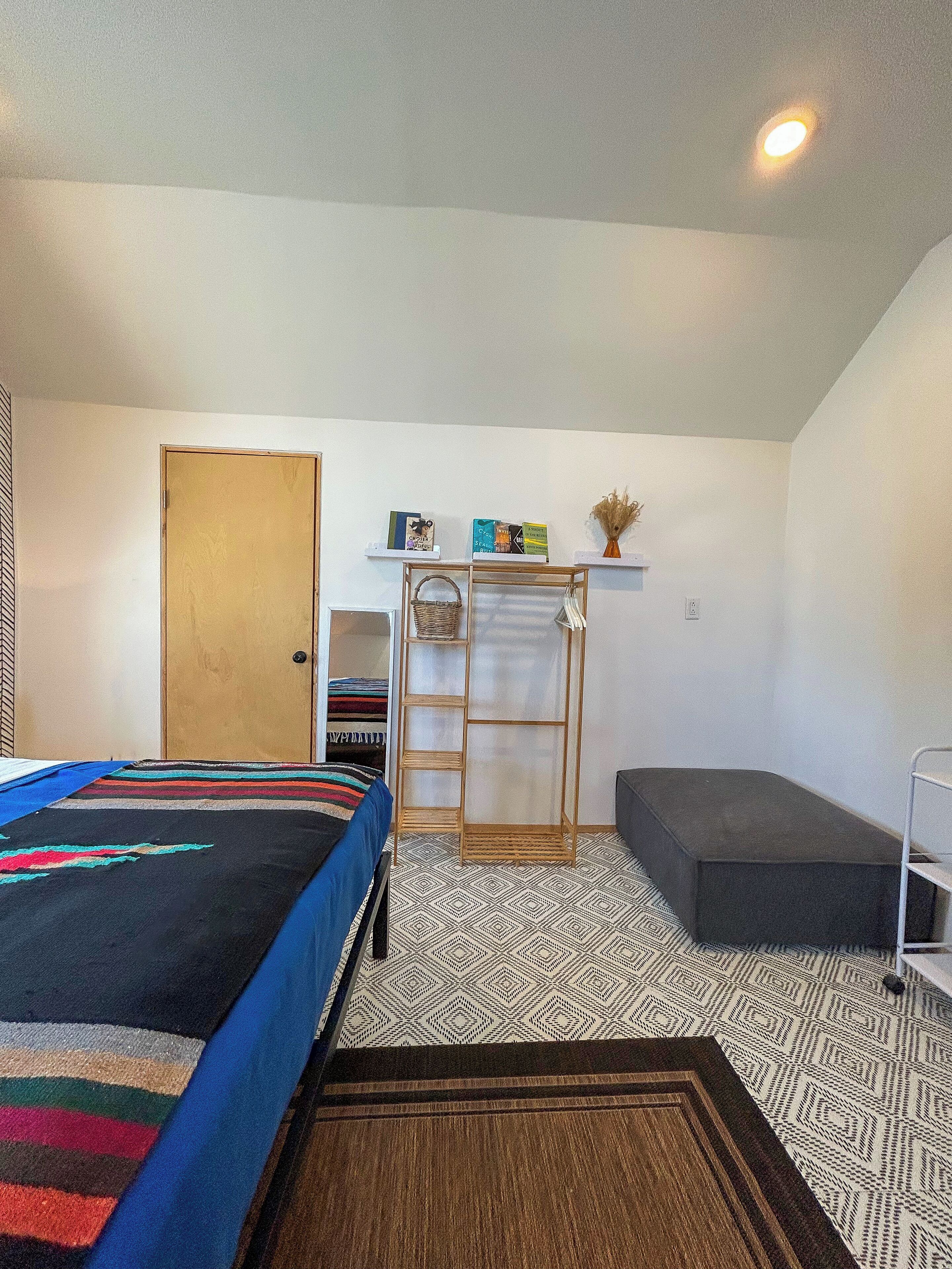 Habitación compacta con cama, un escritorio pequeño con estantes, un banco y piso con diseño.