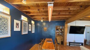 Ein Essbereich mit Holztisch und -stühlen, einer blauen Wand mit gerahmten Bildern, einer Decke mit sichtbaren Balken und einem gefliesten Boden.