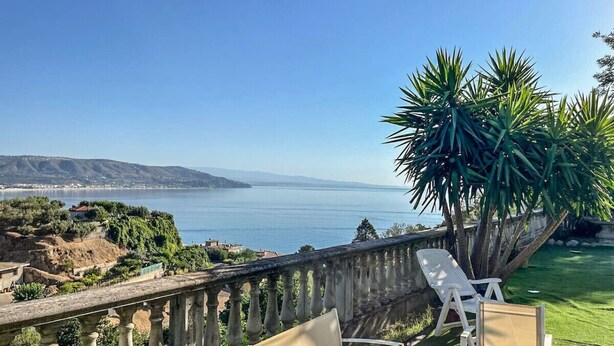 Ein Balkon mit Meerblick, eine Palme und zwei weiße Lounge-Sessel.