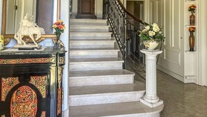 Eine imposante Marmortreppe, eine weiße Säule mit Blumenvase und ein Spiegel mit dekorativem Rahmen.