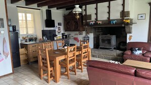 Een knus interieur met houten keukenkastjes, een eettafel en stoelen. Er is een open haard en een bank in de woonkamer.