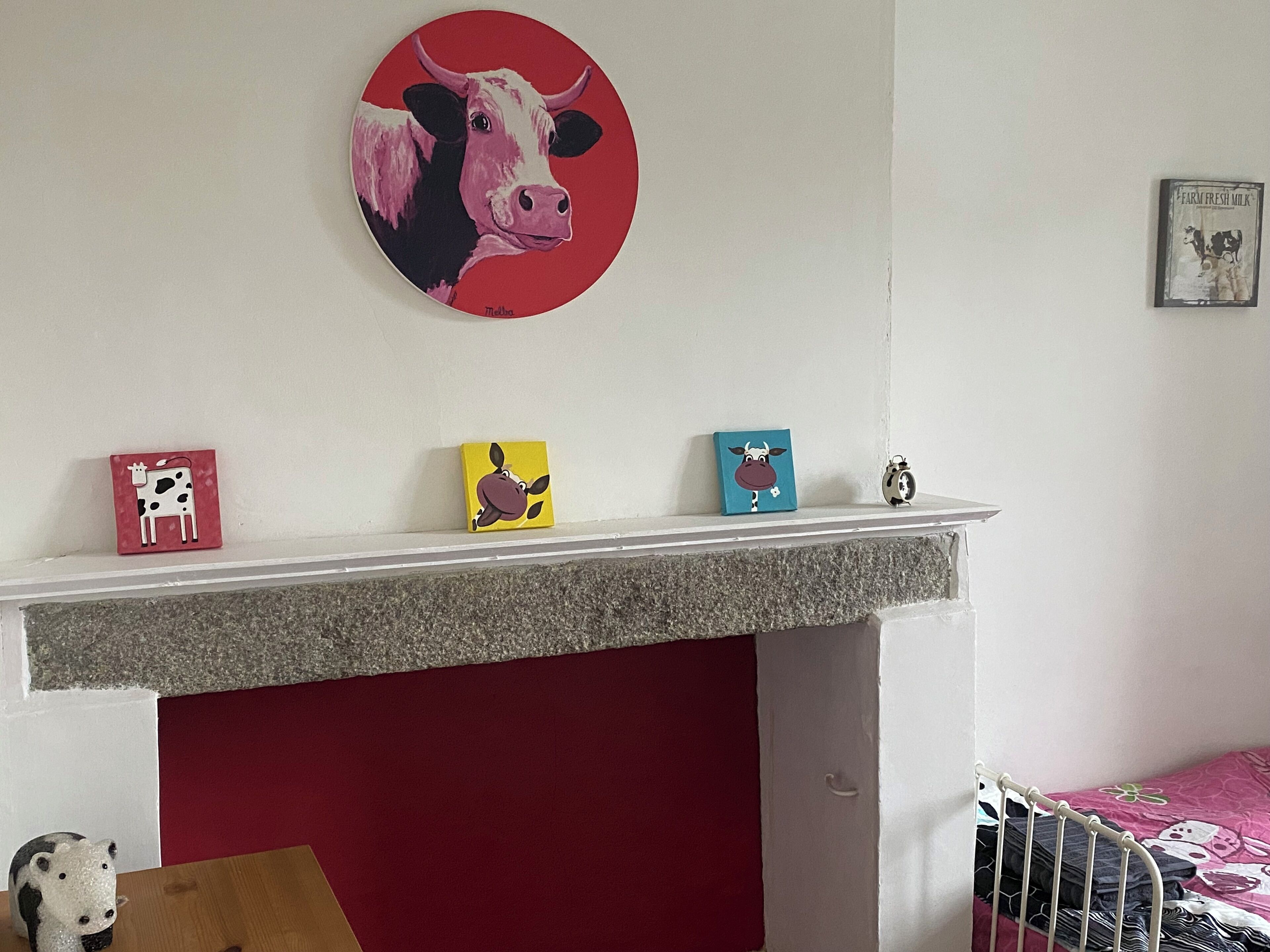 Een kamer met een open haard, een rode muur en een plank met vier ingelijste kunstwerken van koeien.