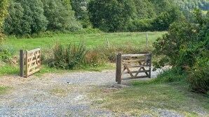 Een landelijk landschap met een grindpad dat naar een houten poort leidt.