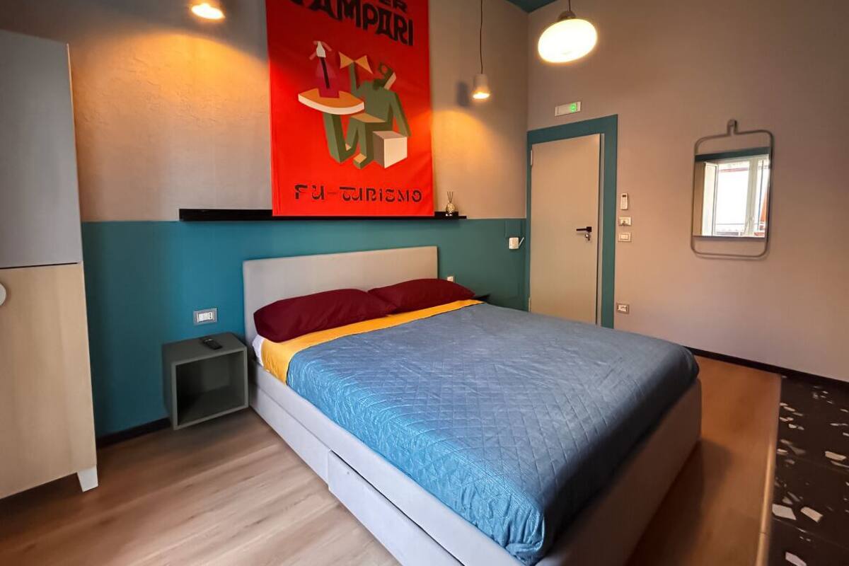 A modern hotel room with a bed, a nightstand, a red poster, and a window.