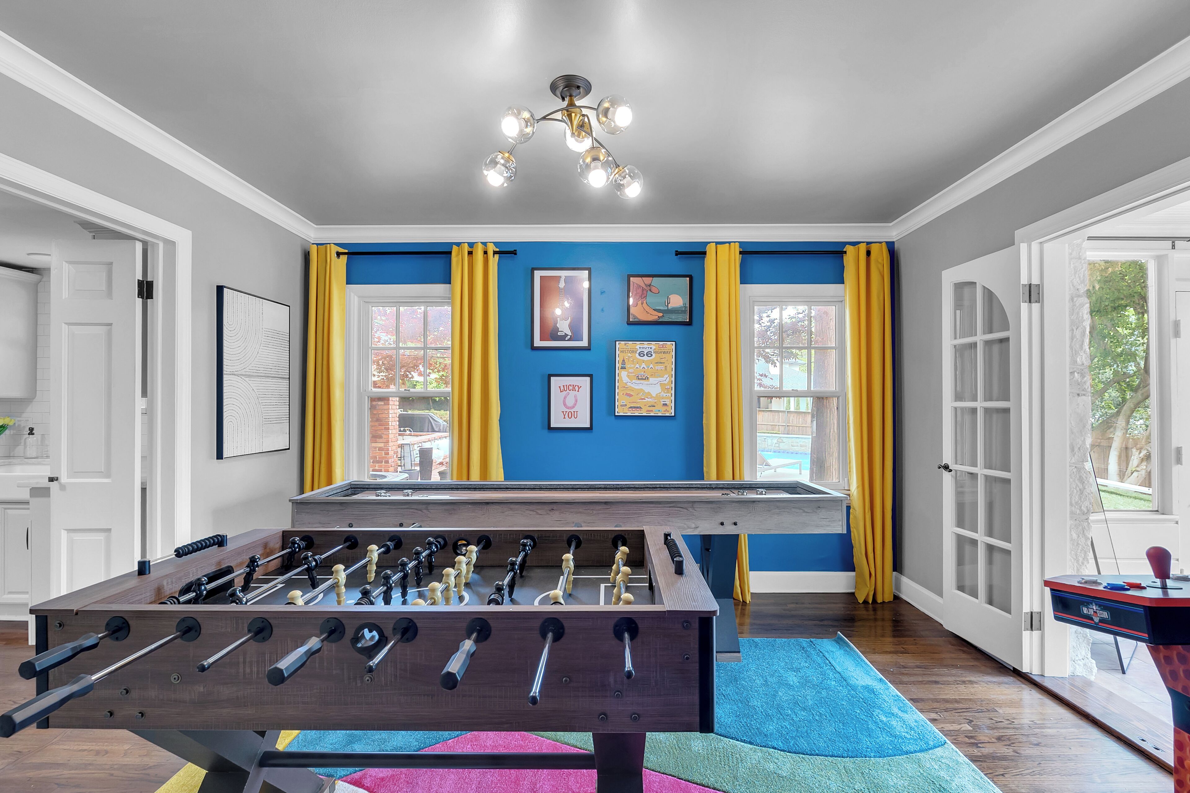 A room with a foosball table, a blue accent wall, yellow curtains, and a ceiling light fixture.