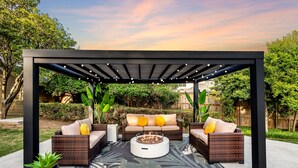 Um pátio externo com pérgola, móveis de vime, lareira e vasos de plantas.