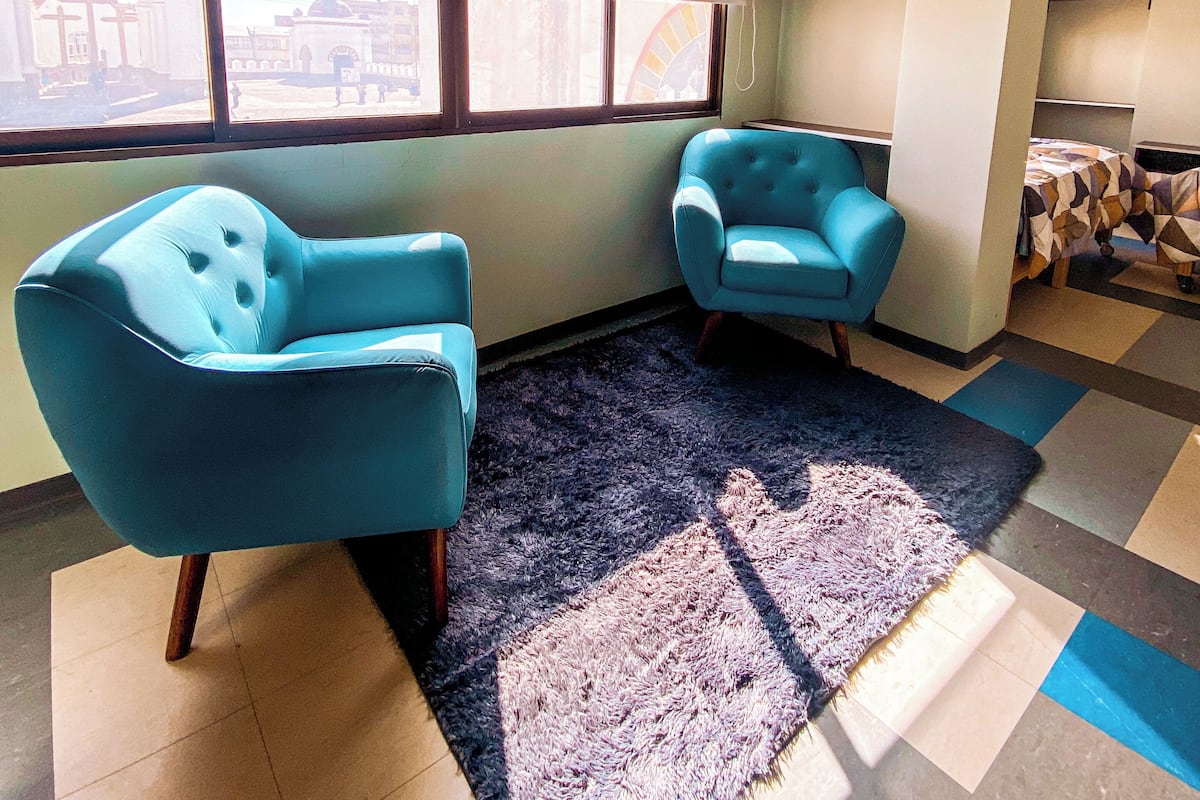 A room with two blue armchairs, a patterned rug, and a large window with a view of a building.