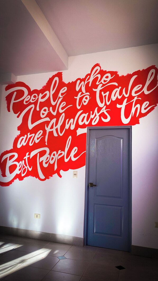 Une pièce dont un mur est décoré d’une fresque rouge sur laquelle on peut lire : « Les personnes qui aiment voyager sont toujours les meilleures », et une porte bleue est fermée.