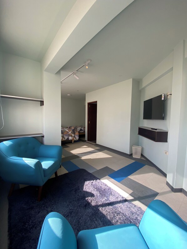 A modern living room with a blue sofa, a flat-screen TV mounted on the wall, and a patterned floor. - Mia Posada Copacabana (Copacabana)