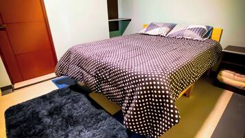 Um quarto com uma cama, um tapete preto e um banco de madeira.