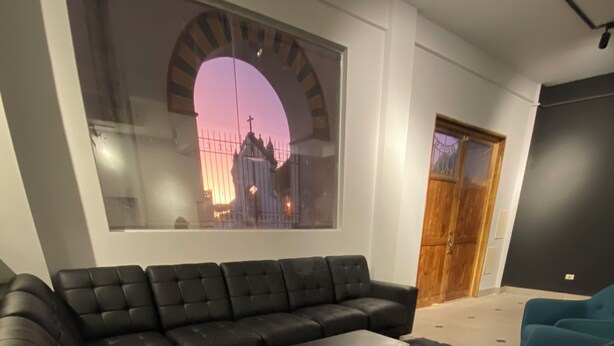 Un salon moderne avec un canapé d’angle, une table basse et une grande fenêtre donnant sur le paysage urbain.