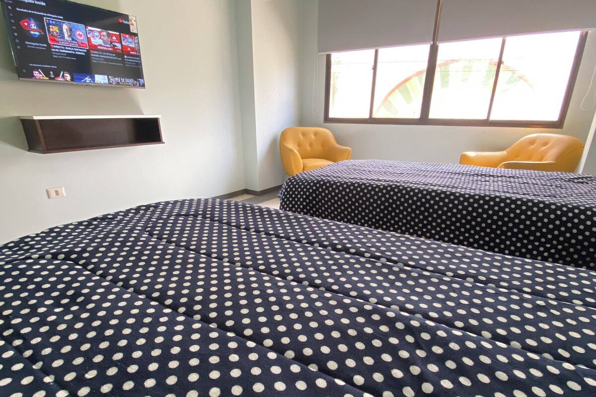 A room with two beds, a TV mounted on the wall, and a window with curtains.