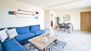 A living room with a blue sofa, a wooden coffee table, and a dining area with a table and chairs. - Cozy Stay with onsite Pool Near Malecon (La Paz)