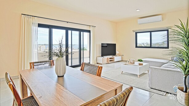 A modern living room with a dining area, large windows, a flat-screen TV, and a potted plant. - Cozy Stay with onsite Pool Near Malecon (La Paz)