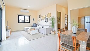 A spacious living room with a grey sofa, a coffee table, and a dining area with a wooden table and chairs. - Cozy Stay with onsite Pool Near Malecon (La Paz)