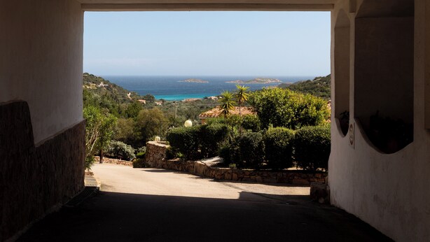 Vista desde un vano a un paisaje costero con cielo despejado, vegetación y islas distantes.